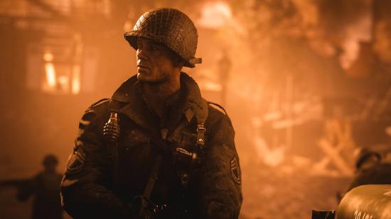 A World War 2 soldier stands in front of a burning building