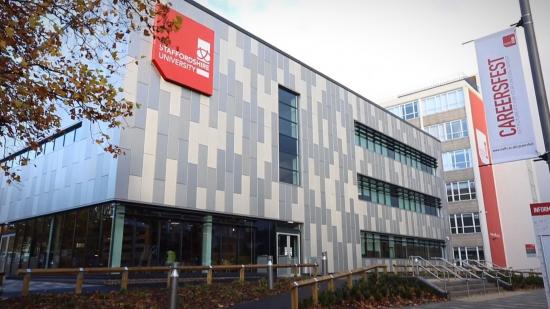 Staffordshire University's campus in Stoke on Trent. A grey and white building with a red sign showing the name of the university