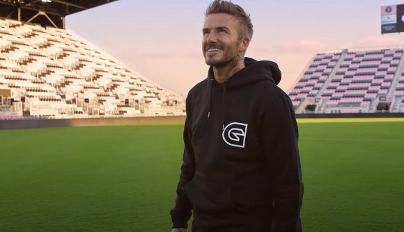 David Beckham, standing in the middle of a football field, wearing a black Guild hoodie