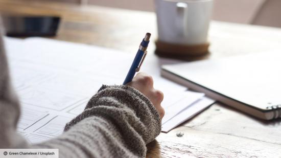 A person holding a pen while writing - a coffee mug is in the background