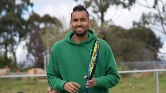 Nick Kyrgios in a green hoodie holding a blue and black tennis racket with yellow string