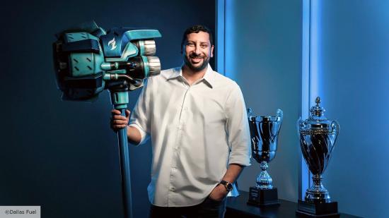 Founder of Team Envy, hastro, poses with a giant hammer in front of two esports trophies