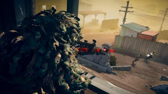 A sniper wearing a ghillie suit aims in on two operators running along the street below
