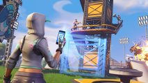 A player in a white hoodie holds up a phone in front of a recently constructed tower in Fortnite