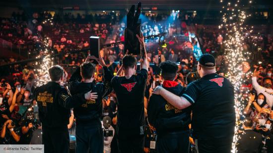 The Atlanta FaZe Call of Duty team hoist the CDL trophy in the air, with their backs to the camera. In the background, a crowd of people cheer