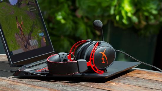 A pair of black and red gaming headphones sitting on top of a laptop which has a game of Fortnite on the display