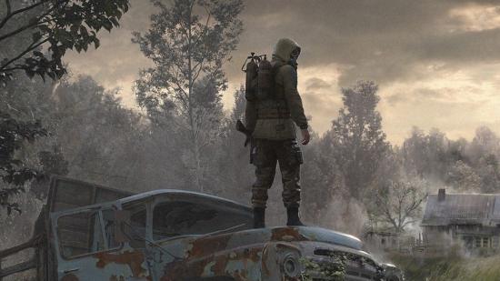 A man wearing a gasmask stands on a car in the middle of Chernobyl
