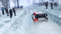 WRC Generations: A car can be seen racing through a snowy hillside with people watching