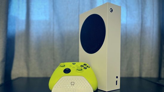 Xbox Series S review: a white Xbox Series S console standing vertically, with a green controller and white controller stand in front of it