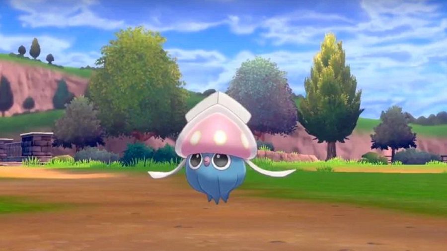 Inkay, a small squid-like Pokémon, levitates over a muddy path through a green field