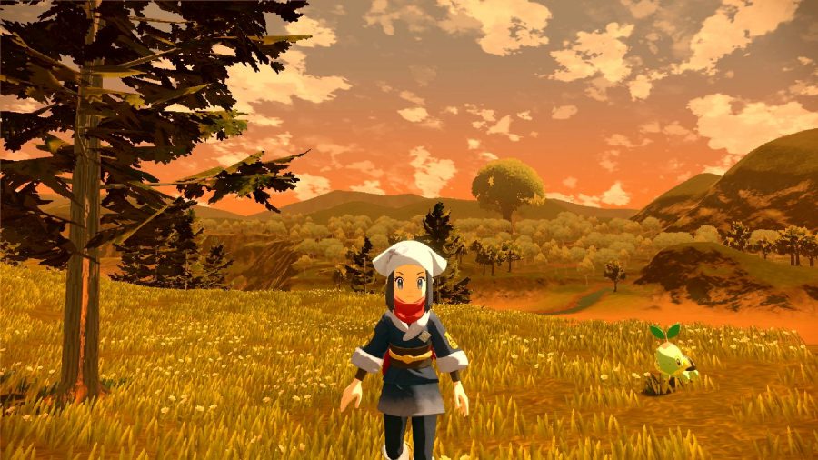 A female Pokémon trainer stands on a hill as the sun sets behind her