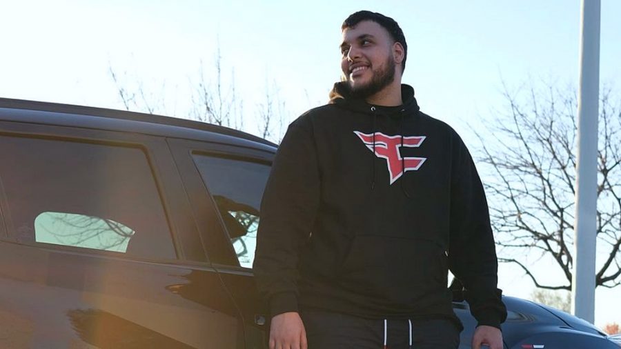 streamer Faxuty standing in front of a black car, wearing a black hoodie with the FaZe Clan logo on it
