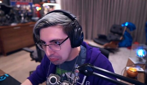 Twitch streamer shroud, sporting blonde hair, black-rimmed glasses, and a purple hoodie, sat at his streaming setup