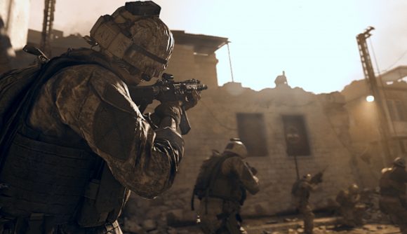 A squad of soldiers in desert camo gear walk through a town with their weapons drawn