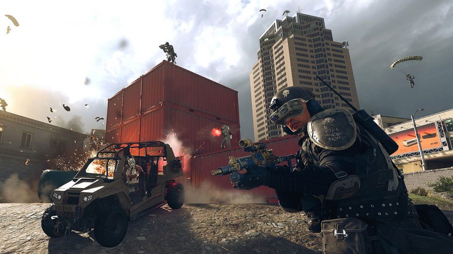 An operator in black military gear draws his weapon. Behind him, another operator is driving a buggy, and players are firing weapons from on top of a stack of red shipping containers