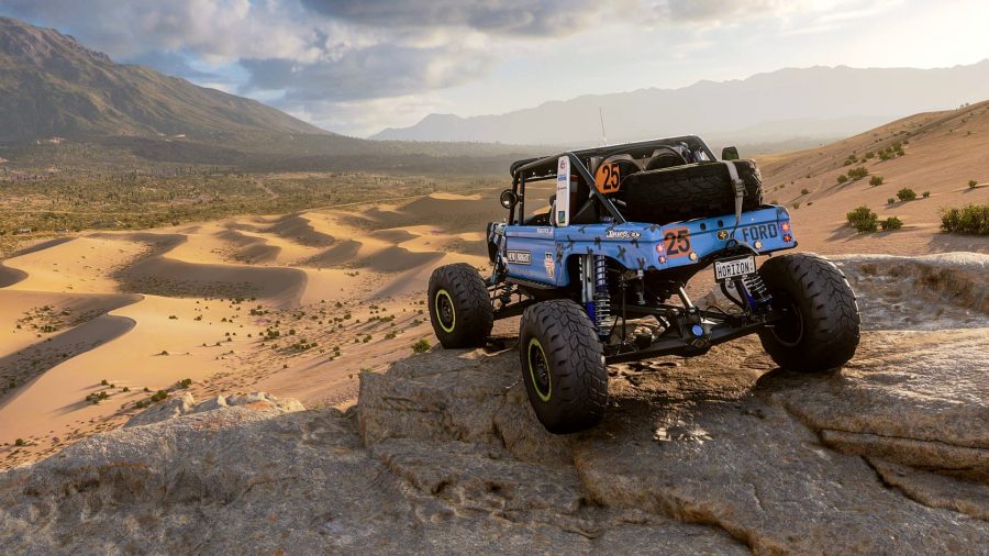 Forza Horizon 5 review: A blue jeep, customised for off-road desert racing, sits atop some rocks, looking out over sand dunes