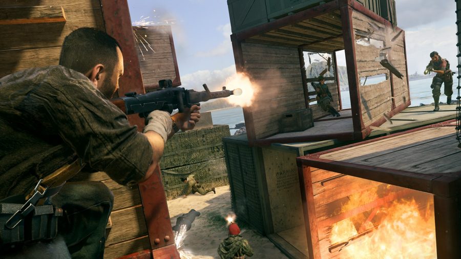 An operator in Call of Duty Vanguard's Shipment map fires a light machine gun at an enemy player while crouched on top of some shipping containers
