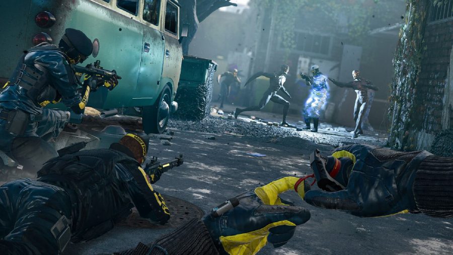 Rainbow Six Extraction Game Pass: Three Operators can be seen crouching and proning from behind a small van.