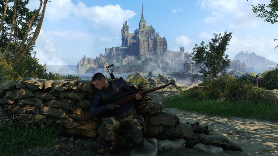 Sniper Elite 5 review: A sniper crouches behind a wall of sandbags. A picturesque castle on an island is in the background
